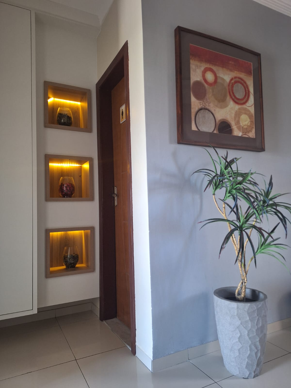 Entrada do consultório, com nichos iluminados e porta de madeira